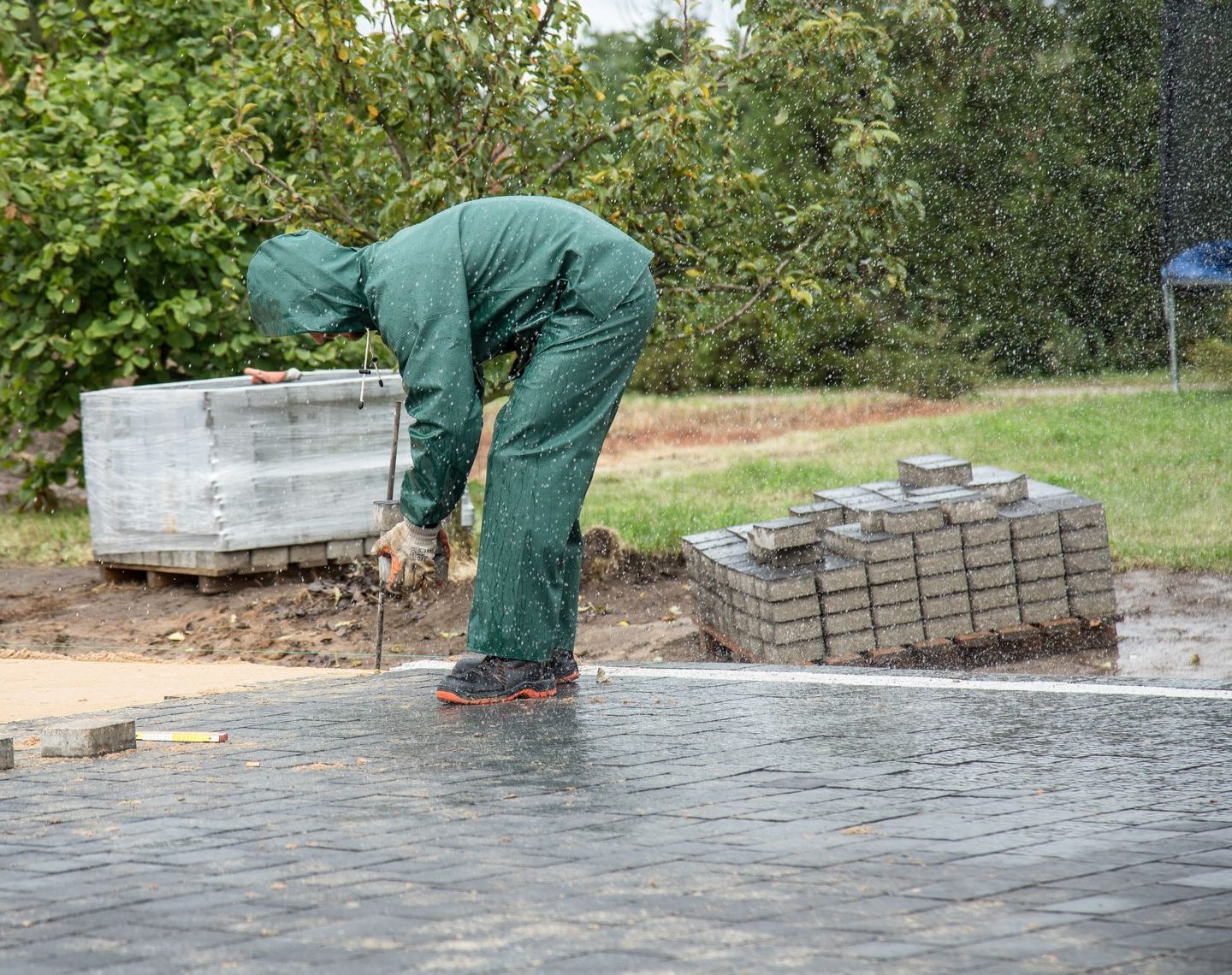 Gepflasterter Weg und Grünfläche an einem Objekt, bei Regen bearbeitet