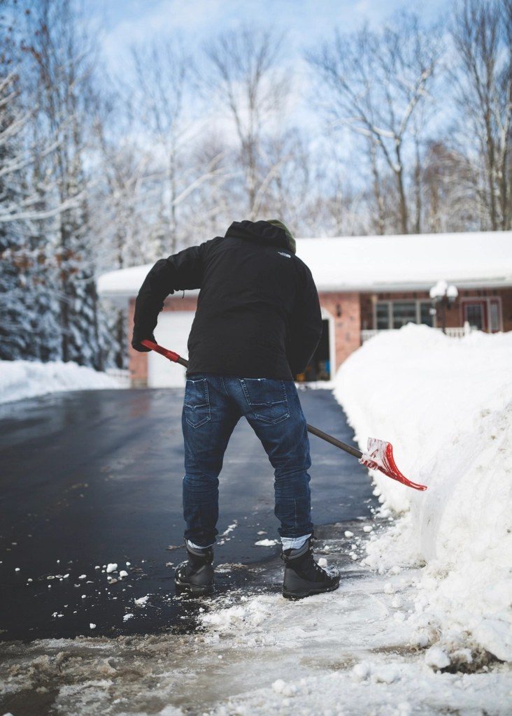 Geräumter Weg neben dem Schneewall, jemand schaufelt die Einfahrt frei